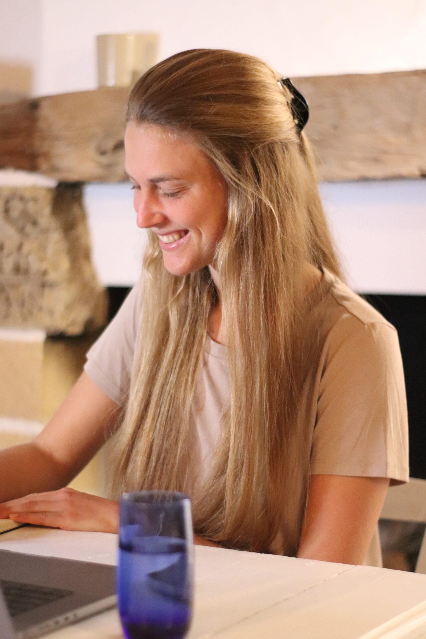 Ein Foto von Jana Buth, sie sitzt an einem Tisch. Vor ihr steht ihr Laptop und ein Glas Wasser.